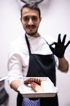 Arabe chef holding a tray with a cooked octopus arm while saying ok with his hand