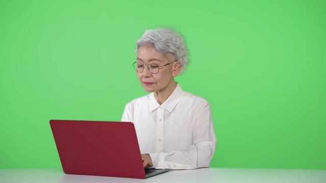 ノートパソコンを使うシニア女性　クロマキー合成用グリーンバック