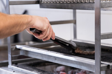 One hand is using large meat tongs to cook on the kitchen grill