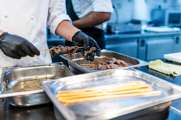 The hands of a chef with black gloves preparing veal skewers for the restaurant service