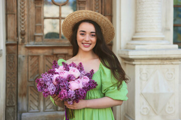 Beautiful woman with bouquet of spring flowers near building outdoors