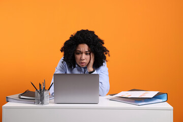 Fototapeta premium Stressful deadline. Sad woman looking at laptop at white desk on orange background