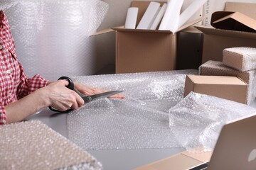 Woman cutting bubble wrap at table in warehouse, closeup