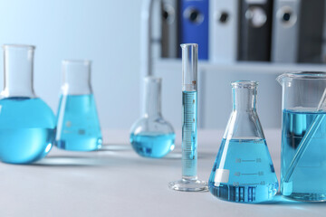 Different laboratory glassware with light blue liquid on table, space for text
