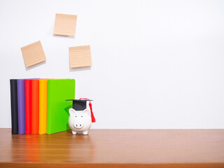 Office desk table, Student creative desktop with colorful hardcover book, Piggy bank with graduation hat, Sticky notes. Copy space for text, Back to school, Education concept