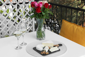 Beautiful roses, glasses of wine and snacks on white table at balcony