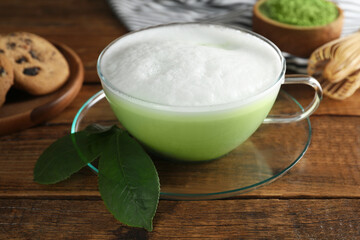 Cup of fresh matcha latte and green leaves on wooden table, closeup