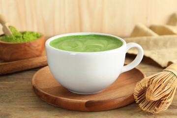 Cup of fresh matcha latte and bamboo whisk on wooden table, closeup