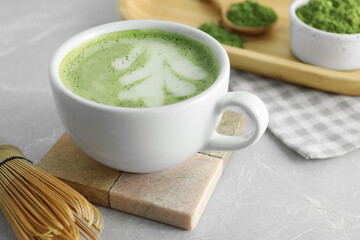 Cup of fresh matcha latte and bamboo whisk on light grey table, closeup
