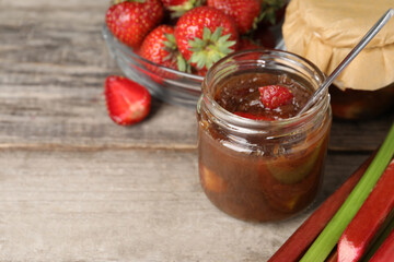 Tasty rhubarb jam, stems and strawberries on wooden table. Space for text