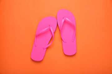 Stylish pink flip flops on orange background, top view