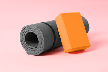 Grey exercise mat and yoga block on pink background