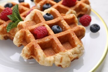 Delicious Belgian waffles with fresh berries and mint on plate, closeup