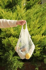 Conscious consumption. Woman with net bag of eco friendly products outdoors, closeup