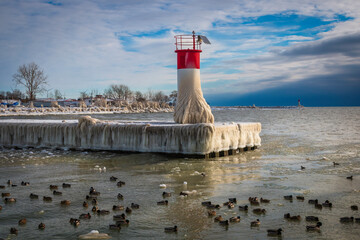 Red and white lighthouse on pier covered with snow and ice during the winter