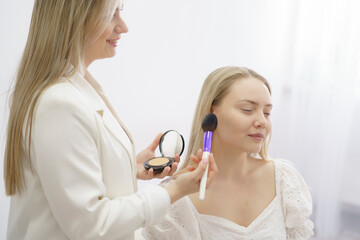 makeup stylist visagiste applying face powder on beautiful model