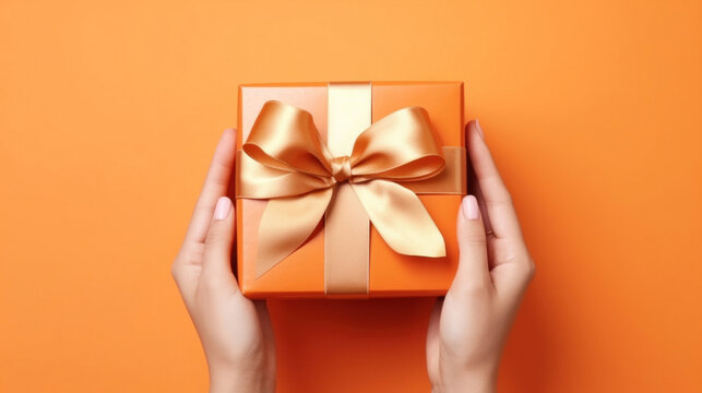 A woman's hands hold an orange gift box with a gold bow and ribbons on a colorful background