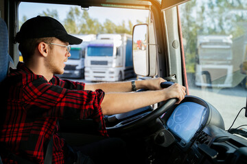 Young Caucasian truck driver with black sports cap with hands on the wheel, closeup