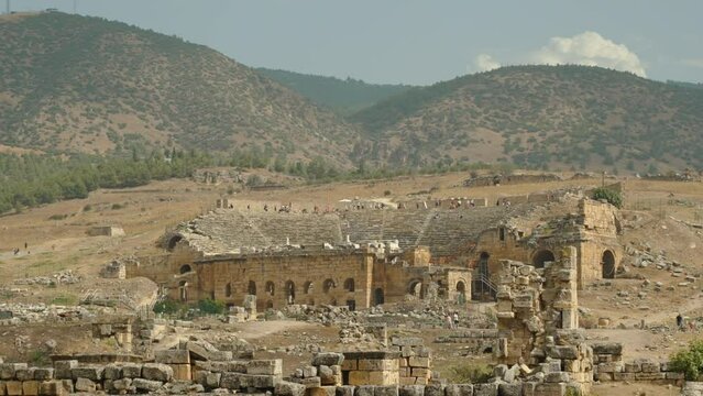 Ancient Ruined Amphitheater in the Distance at the Foot of the Mountain, People on Top of It.