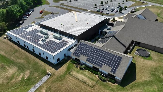 Mega church in America installing solar array to provide clean and renewable green energy for the building. Industrial and shingle roof with workers. Aerial establishing shot.