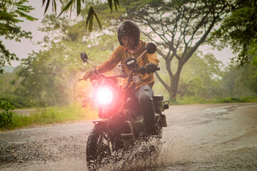 man riding small endurom motorcycle crossing shallow creek among rain falling at forest - 661252963