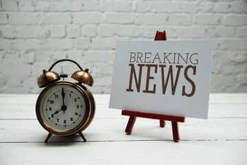 Breaking News text and alarm clock on white brick wall and wooden background