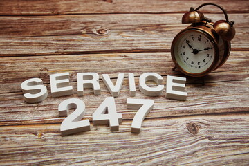 24/7 Service alphabet letters and alarm clock on wooden background