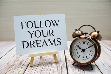 Follow Your Dreams word with alarm clock on wooden background
