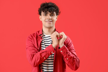 Handsome young man making heart with his hands on red background