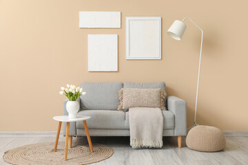 Cozy grey sofa with cushion and vase of tulip flowers on table near beige wall