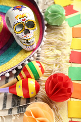 Mexican maracas with sombrero hat, painted skull, serape and flags on yellow background, closeup
