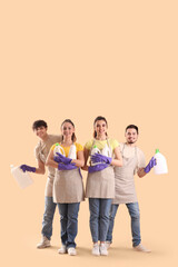 Young janitors with cleaning supplies on beige background