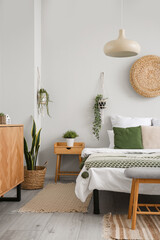 Interior of light bedroom with cozy bed, wooden cabinet and hanging houseplants