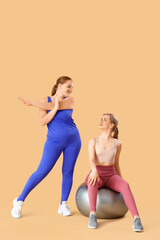 Sporty young women with fitball on beige background