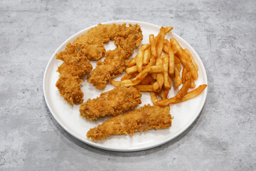 A white plate with crispy chicken breast strips or tenders with seasoned French fries on the side.