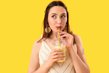Young woman drinking smoothie on yellow background, closeup