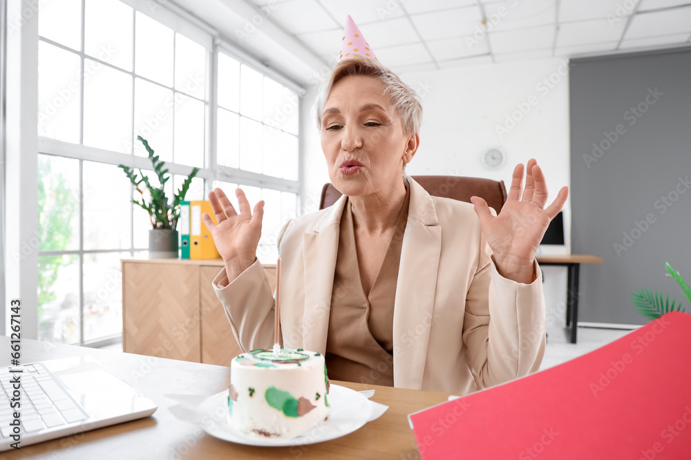 Poster mature woman with birthday cake making wish in office