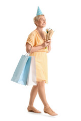 Mature woman with tulips and bags of birthday gifts on white background