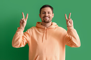 Handsome man showing victory gesture on green background