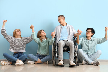 Group of teenagers with boy in wheelchair holding hands near blue wall