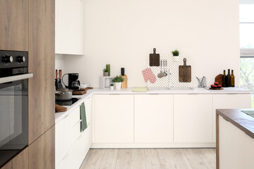 Interior of light kitchen with cutting boards, pegboard, sink and utensils on white counter