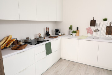 Interior of light kitchen with cutting boards, pegboard, sink and electric stove on white counters