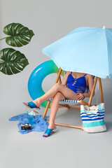 Young woman sitting in deckchair with glass of cocktail and inflatable ring on grey background