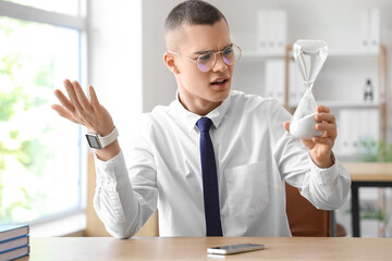 Displeased young businessman with hourglass in office