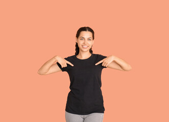 Fototapeta na wymiar Young woman pointing at her black t-shirt on beige background