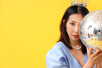 Fashionable beautiful young Asian woman with disco ball on yellow background