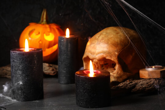 Composition with burning candles and skull for Halloween celebration on black background, closeup