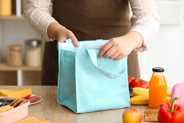 Mother packing meal for school lunch on table in kitchen