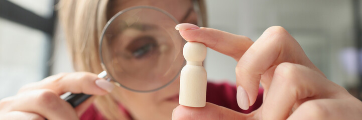 Focused woman examines small wooden figure with magnifier