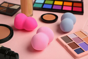 Makeup sponges and different cosmetics on pink background, closeup